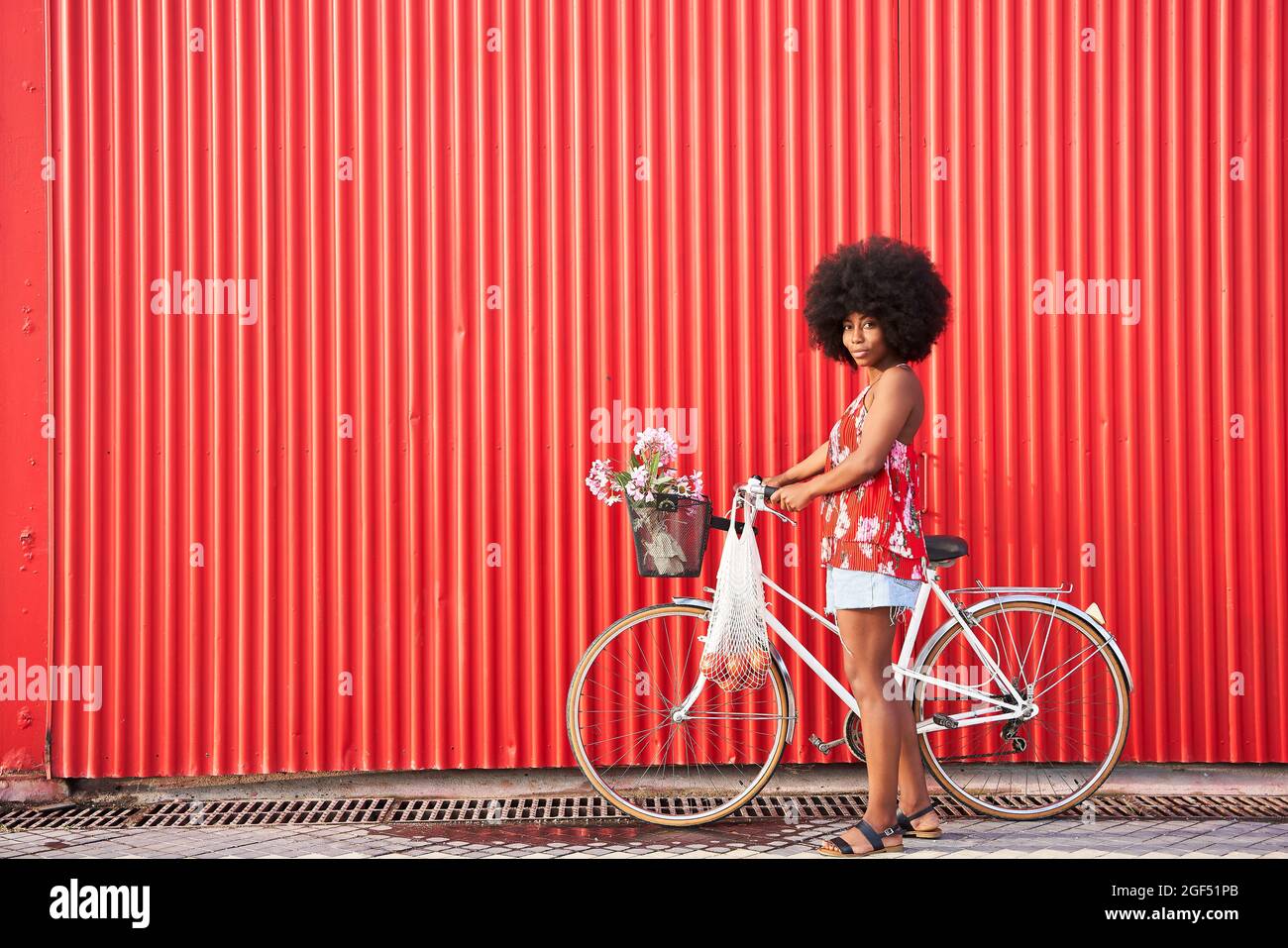 Afro woman with bicycle standing by red corrugated wall Stock Photo