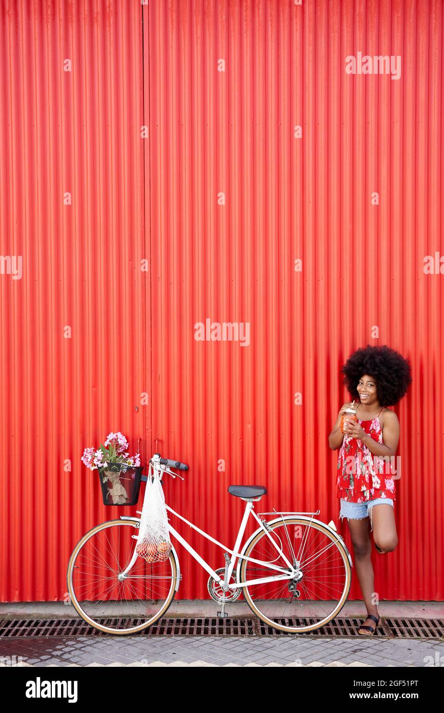 Young woman standing by bicycle in front of red wall Stock Photo