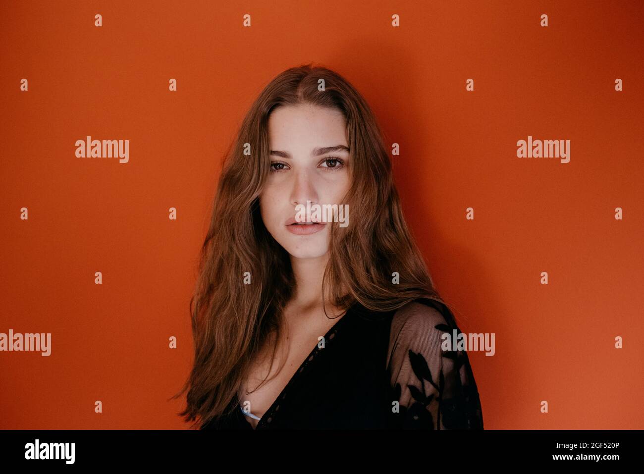 Beautiful young woman with long brown hair against red background Stock Photo