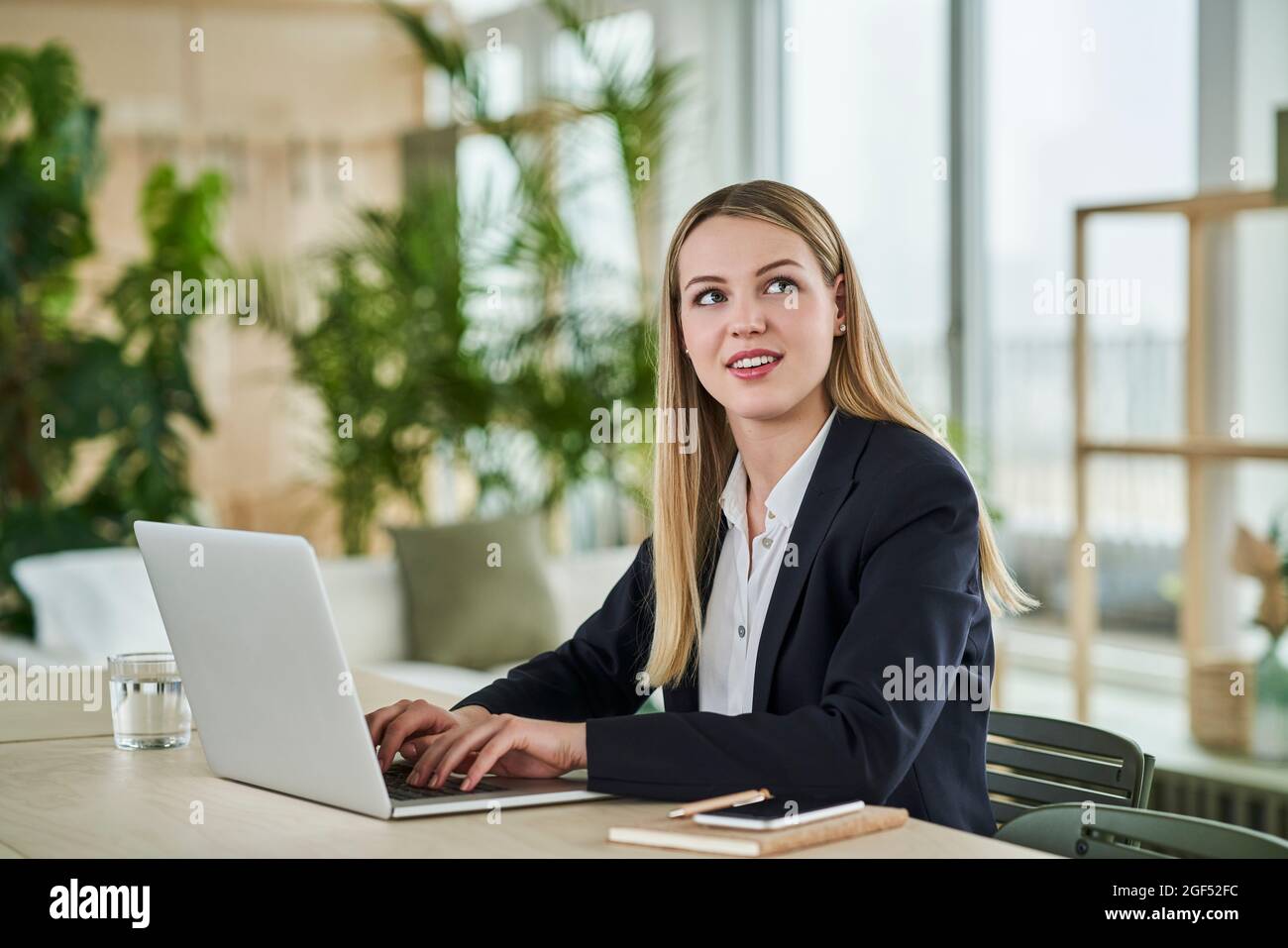 Blond female intern looking away while sitting with laptop at desk in office Stock Photo