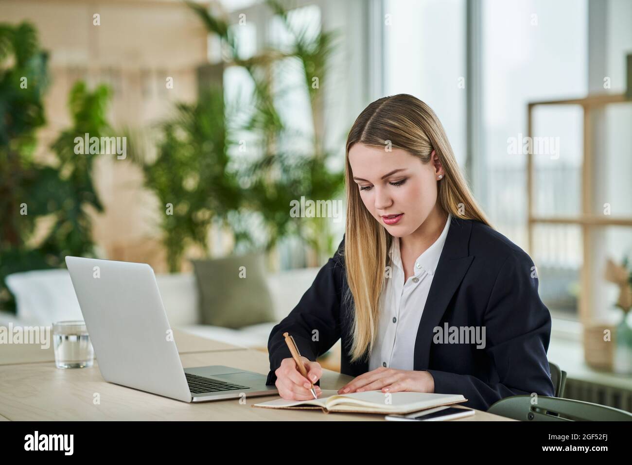 Female trainee writing in dairy while sitting at desk in office Stock ...