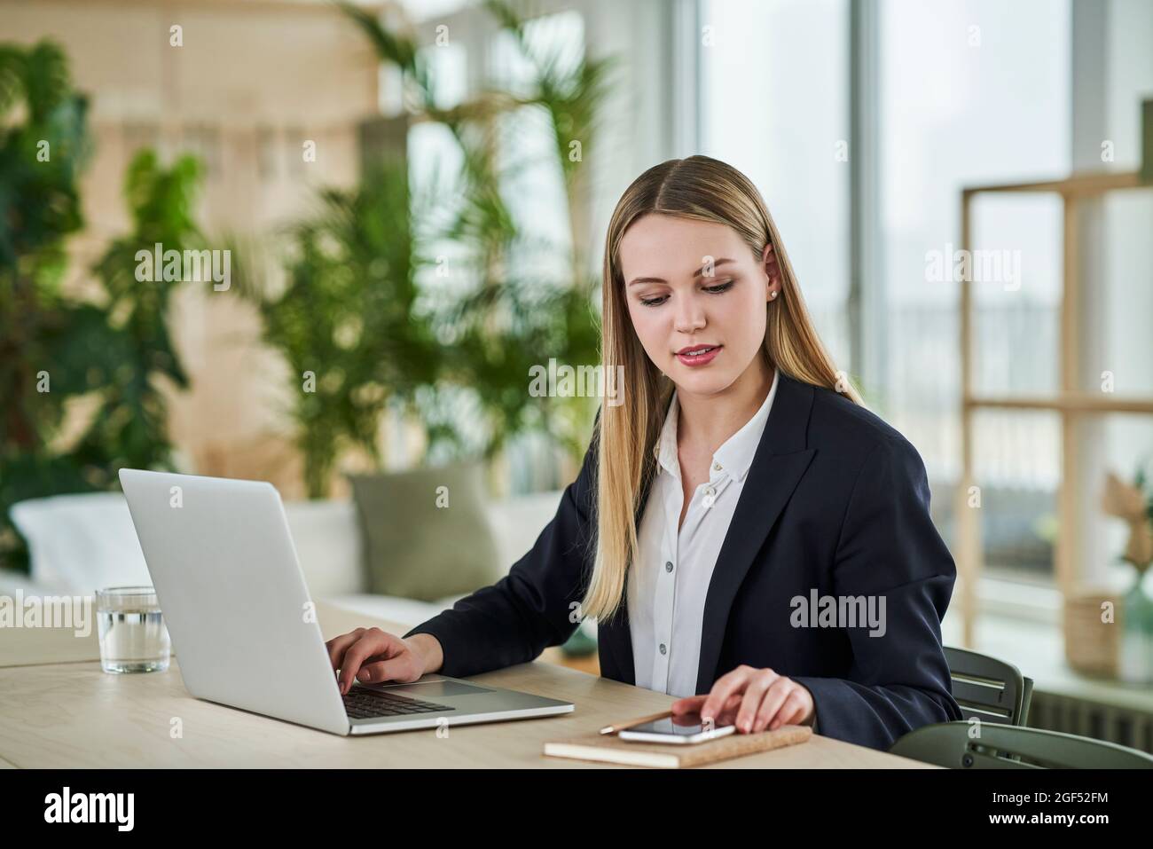 Female intern using smart phone while sitting with laptop in office Stock Photo