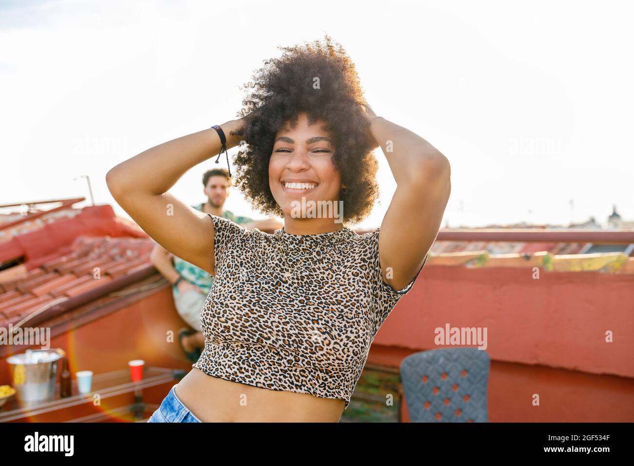 Cheerful Afro woman dancing with hands in hair on rooftop Stock Photo