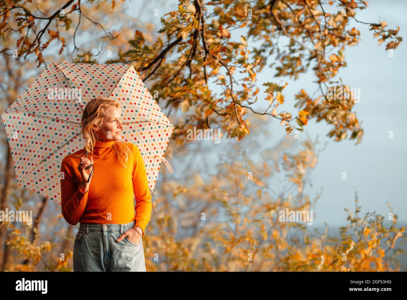 Woman looking away while standing with hand in pocket holding umbrella on sunny day Stock Photo