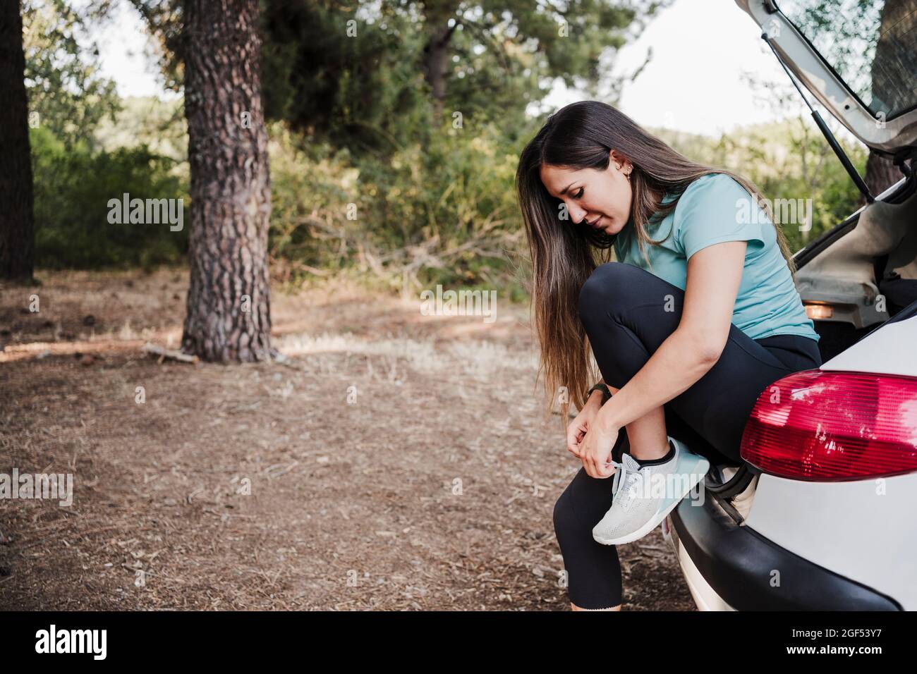 Young woman tying shoelace while sitting in car trunk Stock Photo