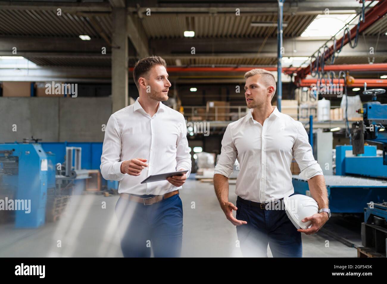 Male professionals discussing while walking in factory Stock Photo