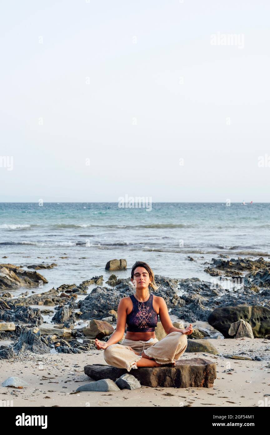 Woman doing lotus position on rock at beach Stock Photo