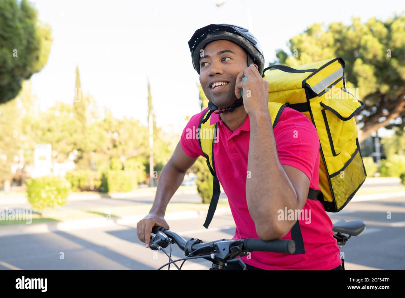Smiling delivery man talking on smart phone while leaning on bicycle Stock Photo