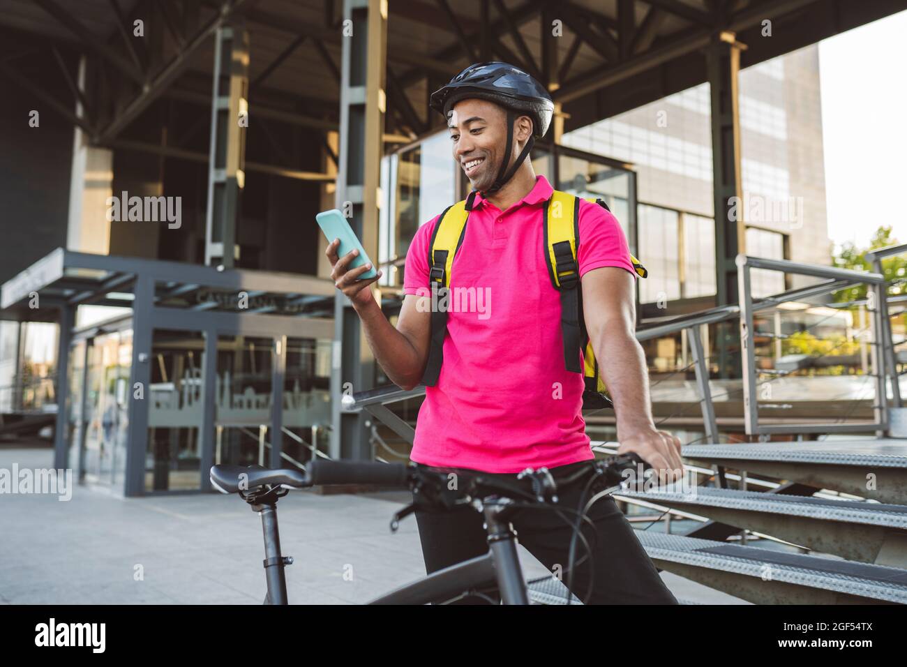 Smiling delivery man text messaging through smart phone while standing with bicycle Stock Photo
