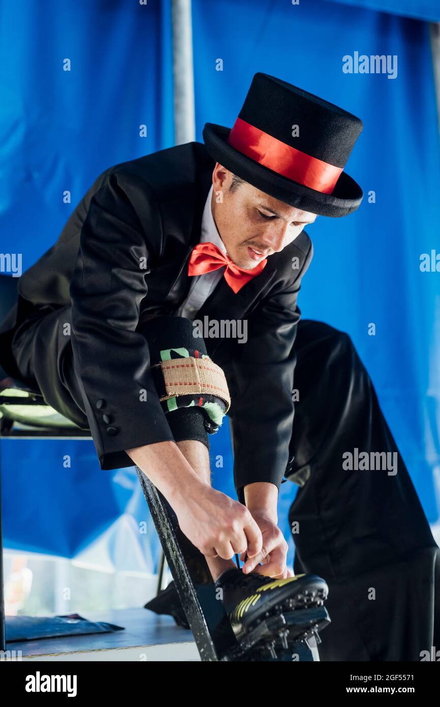 Male performer with stilts tying shoelace at tent Stock Photo
