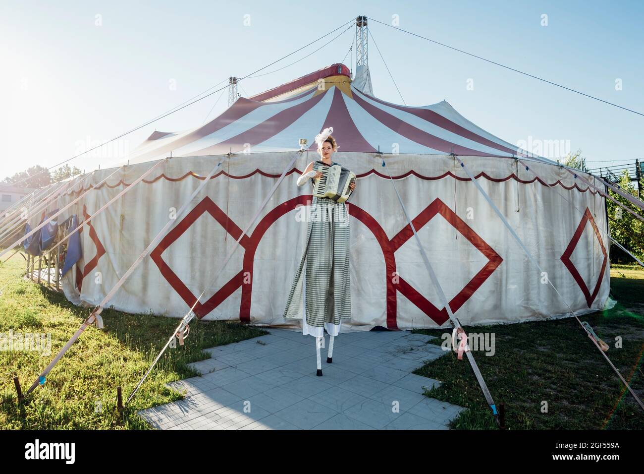 Female circus performer playing accordion while standing on stilts in