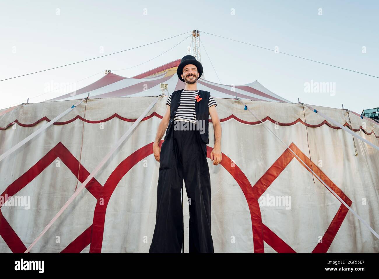 Male artist standing with stilts in front of circus tent Stock Photo