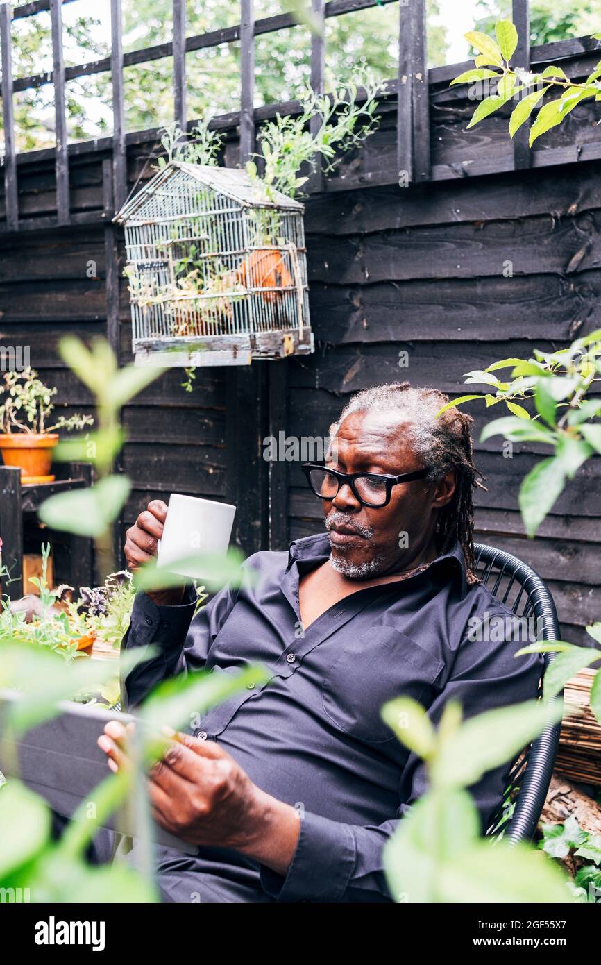 Senior businessman using digital tablet while holding mug in backyard Stock Photo