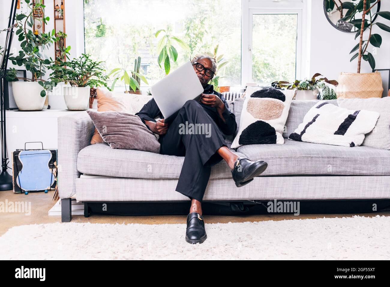 Senior businessman examining laptop while sitting on sofa at home Stock Photo