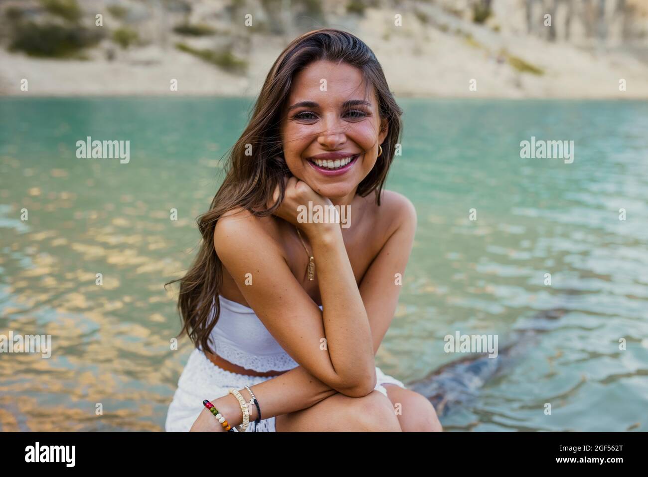 Beautiful young woman with hand on chin sitting at Pantano de Santa Ana, Castillonroy, Spain Stock Photo