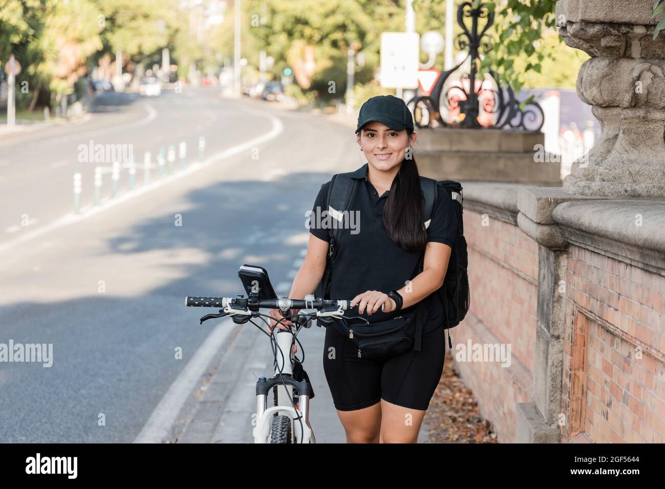 Smiling young female delivery person wheeling bicycle Stock Photo