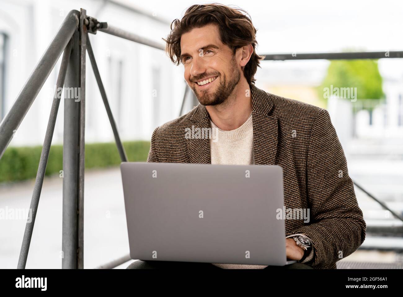 Smiling businessman looking away while sitting with laptop Stock Photo