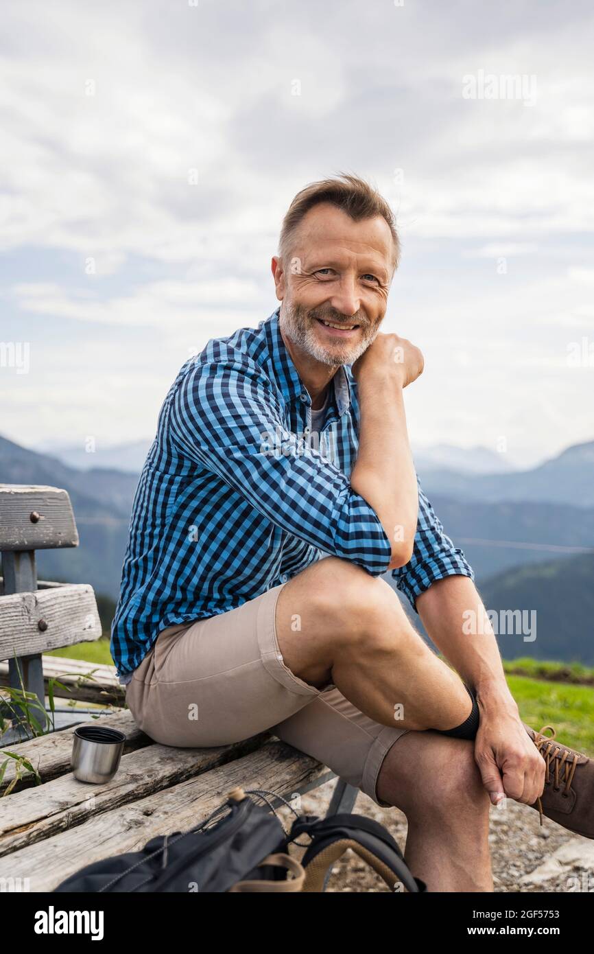 Smiling man sitting with legs crossed at knee on bench Stock Photo