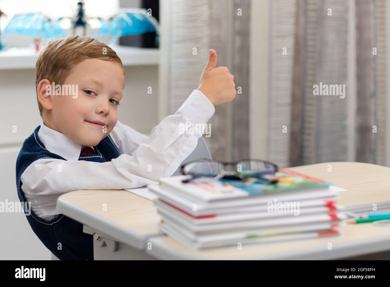 Cute boy first grader in school uniform at home during a break fooling around while sitting at his desk. Selective focus. Close-up. Portrait Stock Photo