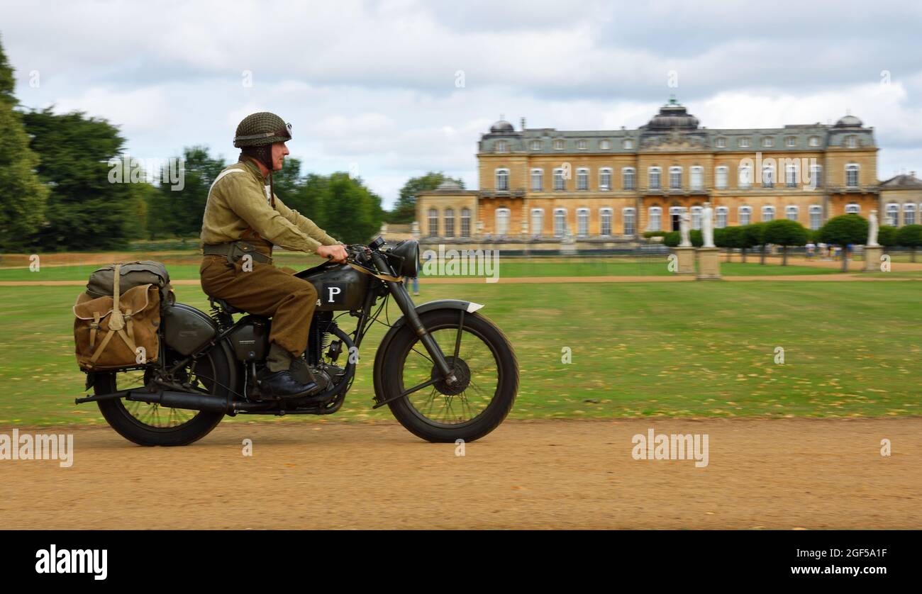World War 2 despatch rider in uniform on classic  motorcycle riding past stateley home. Stock Photo