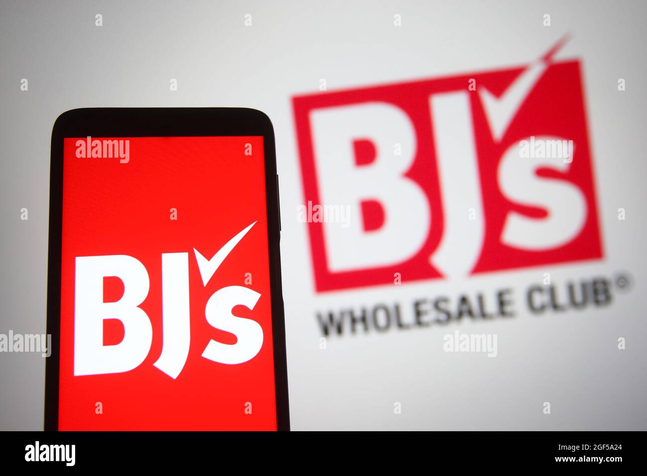 In this photo illustration, BJ's Wholesale Club Holdings logo is seen displayed on a smartphone and a pc screen. Stock Photo