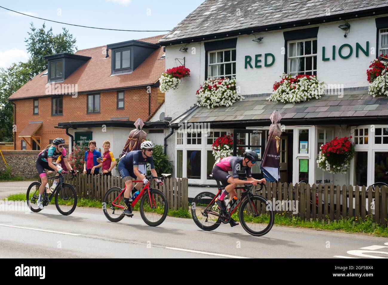 Cyclists taking part in the 2021 Victor Berlemont Trophy road race around Woodcote in Oxfordshire pass the Red Lion public house in Woodcote Stock Photo