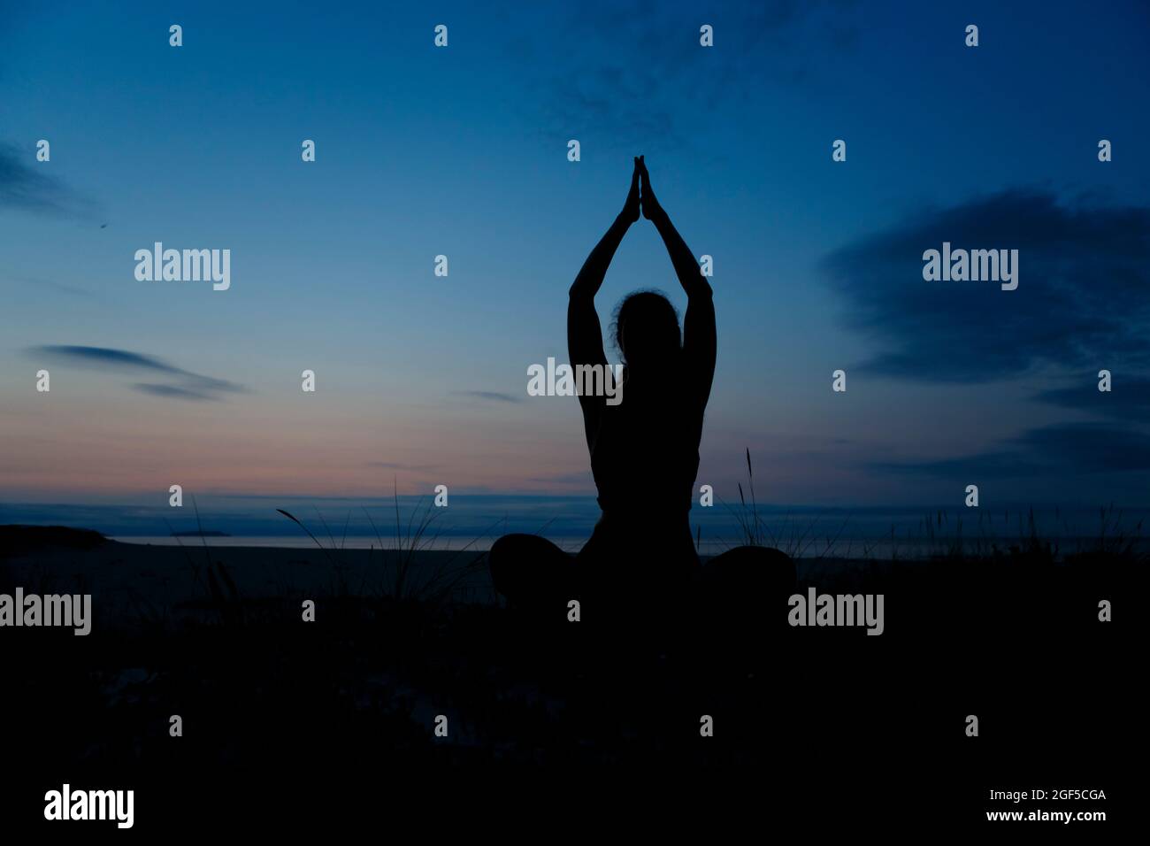 Silhouette of young woman practicing yoga, lotus position, and meditating on the beach Stock Photo