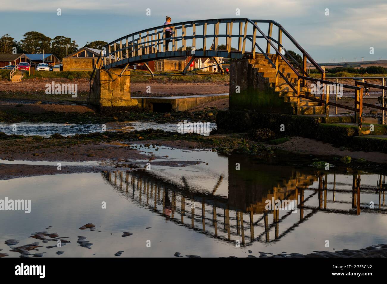 Dunbar, East Lothian, Scotland, United Kingdom, 23rd August 2021. UK Weather: sunset at Belhaven Bay. A warm evening with a colourful sky as the sun sets at low tide with a woman standing on the so-called 'Bridge to Nowhere' Stock Photo