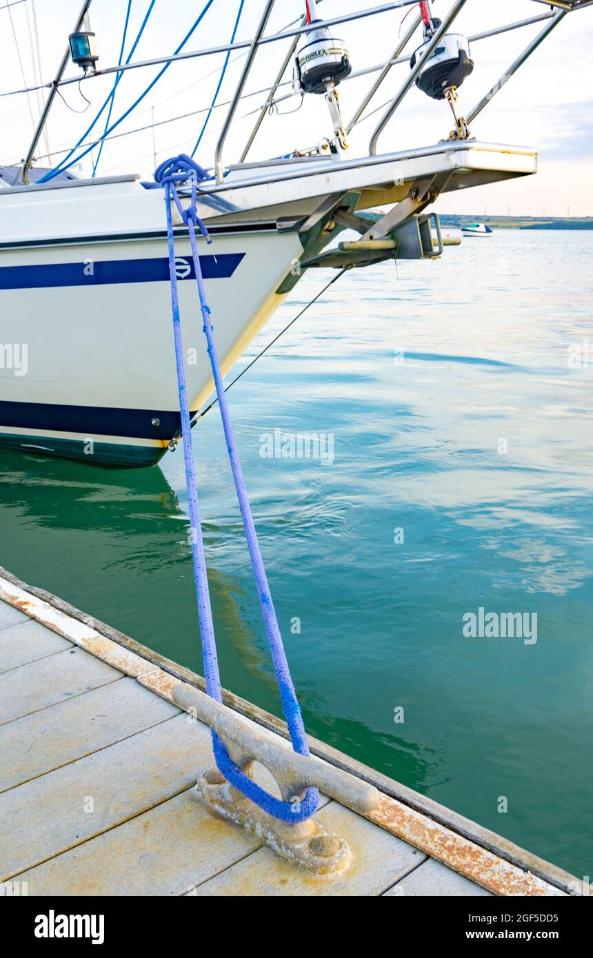 A boat moored to a pontoon, attached via a blue rope tied around a cleat. Stock Photo