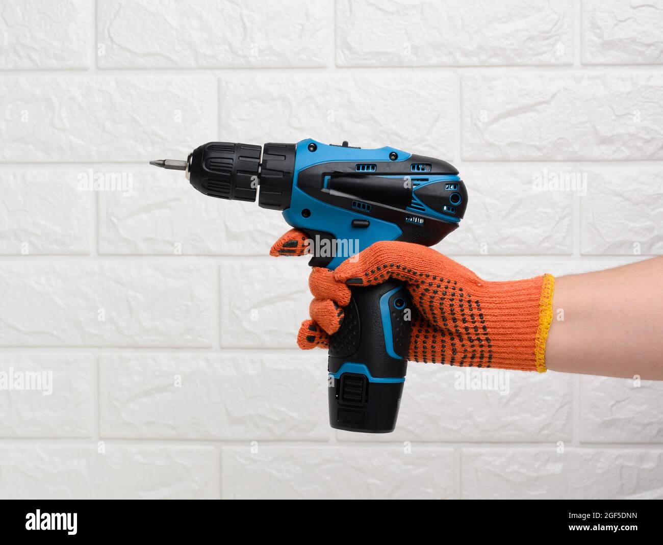 https://c8.alamy.com/comp/2GF5DNN/hand-in-a-textile-glove-holds-a-portable-drill-on-a-battery-against-a-background-of-a-white-brick-wall-2GF5DNN.jpg