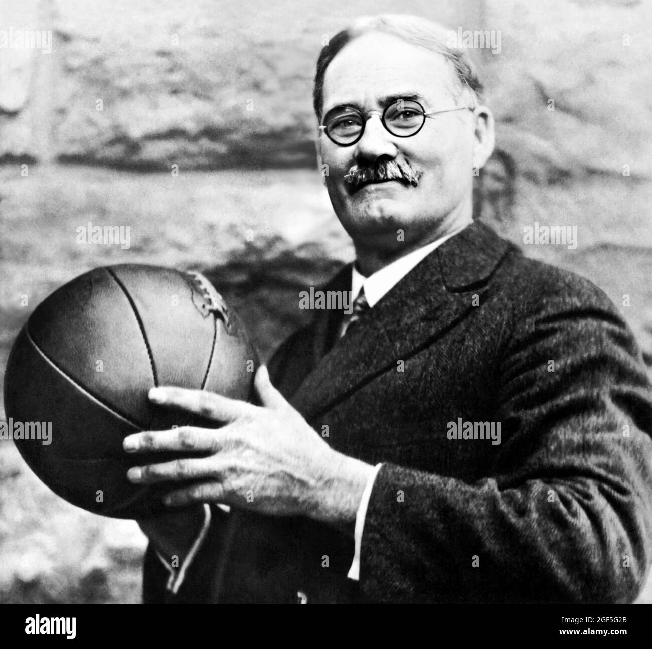 1930 ca , USA : The american Doctor JAMES A. NAISMITH ( 1861 - 1939 ), born-canadian, inventor of BASKETBALL sport . he wrote the original basketball rule book and founded the University of Kansas basketballs program . Unknown photographer . - BASKET - JIM THE DOC - SPORT  -  PALLACANESTRO - INVENTORE - INVENZIONE - INVENTION - DISCIPLINA SPORTIVA - Dottore - HISTORY - FOTO STORICHE - PORTRAIT - RITRATTO - prato - grass - meadow - palla - ball - cravatta - tie - occhiali da vista - lens ----  Archivio GBB Stock Photo