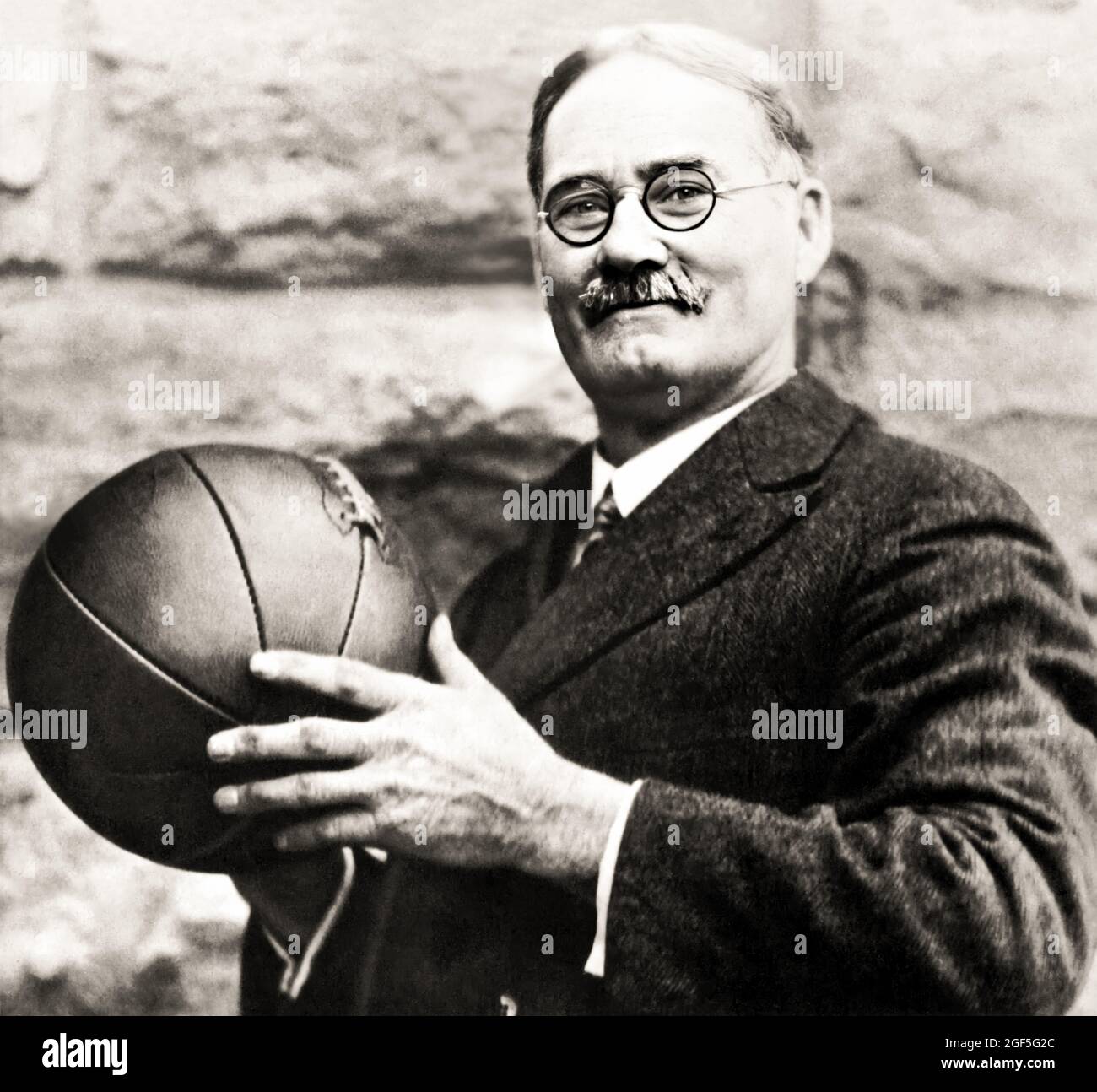 1930 ca , USA : The american Doctor JAMES A. NAISMITH ( 1861 - 1939 ), born-canadian, inventor of BASKETBALL sport . he wrote the original basketball rule book and founded the University of Kansas basketballs program . Unknown photographer . - BASKET - JIM THE DOC - SPORT  -  PALLACANESTRO - INVENTORE - INVENZIONE - INVENTION - DISCIPLINA SPORTIVA - Dottore - HISTORY - FOTO STORICHE - PORTRAIT - RITRATTO - prato - grass - meadow - palla - ball - cravatta - tie - occhiali da vista - lens ----  Archivio GBB Stock Photo