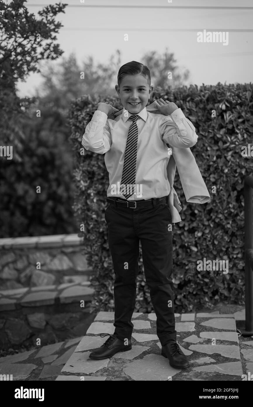 Vertical grayscale shot of an adorable male child in a formal suit outfit posing Stock Photo