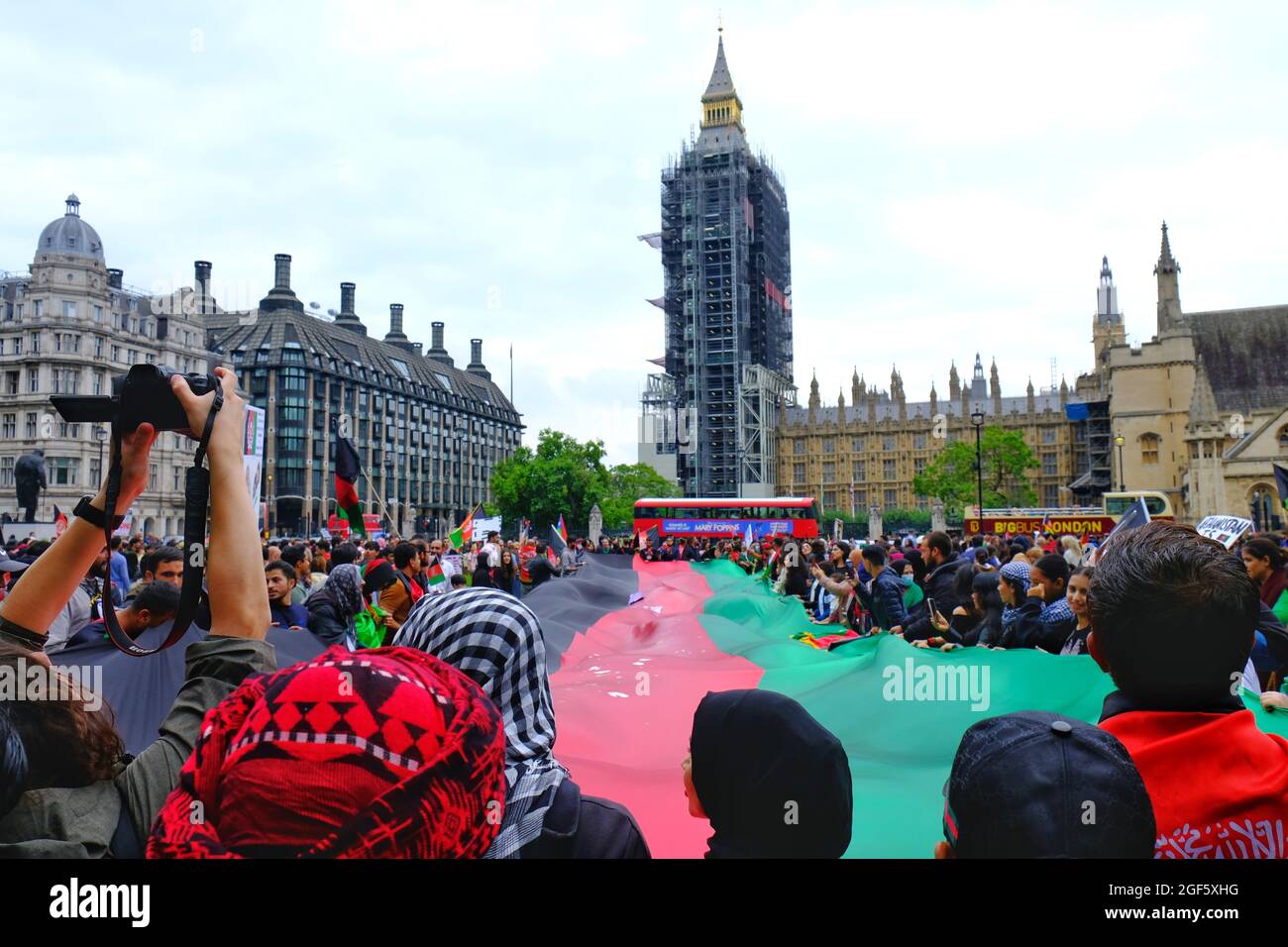 London, UK. Protesters bearing an enormous Afghan flag make their way onto Parliament Green in a show of solidarity after the Taliban takeover. Stock Photo