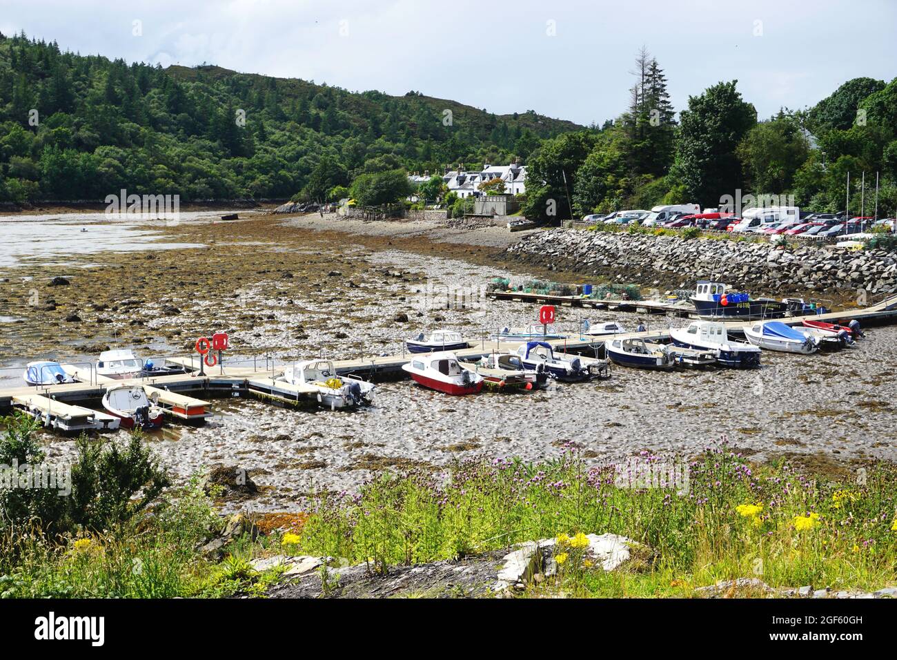 Boats and the dock they're moored to sit on the tide flats at low tide in the harbor at the Village of Plockton in the Scottish Highlands. Stock Photo