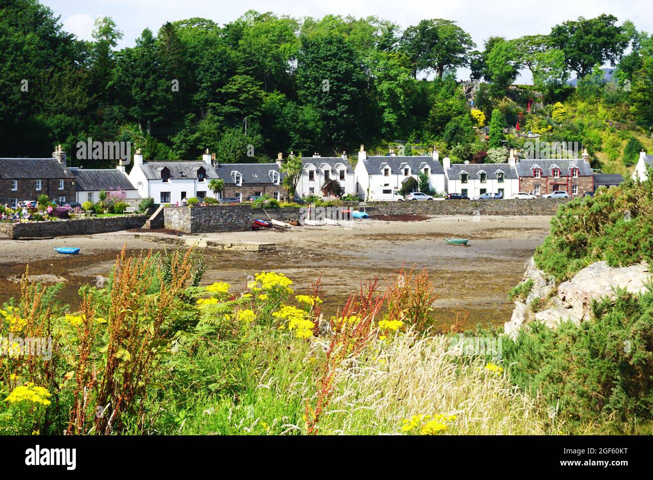 A row of historic whitewashed buildings lines the shore in the Village of Plockton as low tide reveals the muddy tideflats in the middle distance Stock Photo