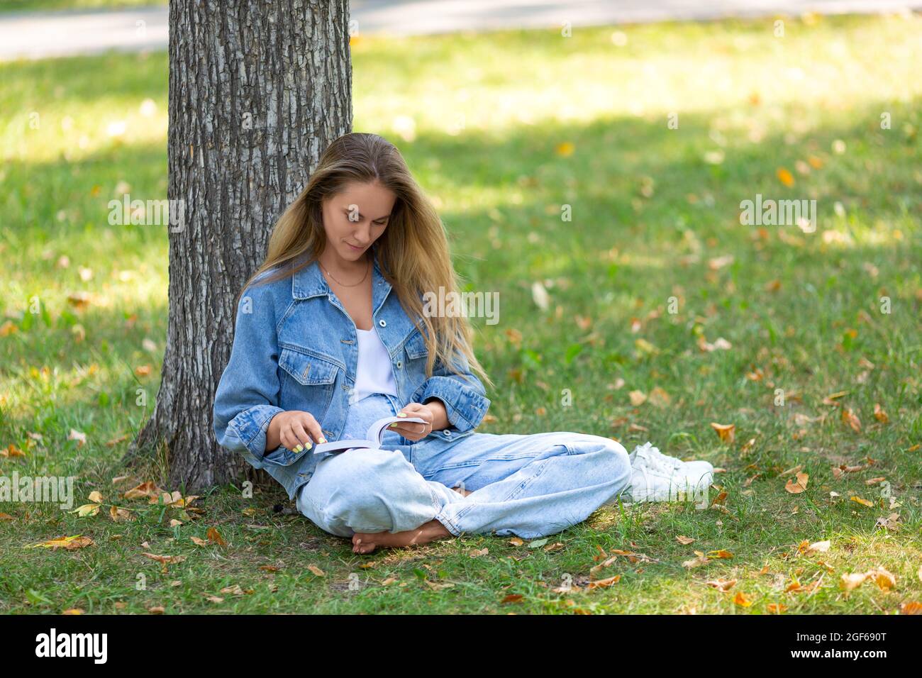 Woman with a book in the park. She sits on the grass in the park and reads a story. The concept of rest from gadgets, smartphones and the Internet. Di Stock Photo