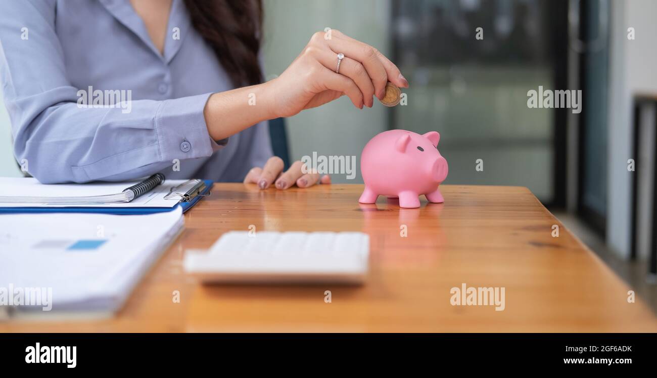 Close up hand of woman putting money coin into pink piggy bank for saving money wealth and financial concept Stock Photo
