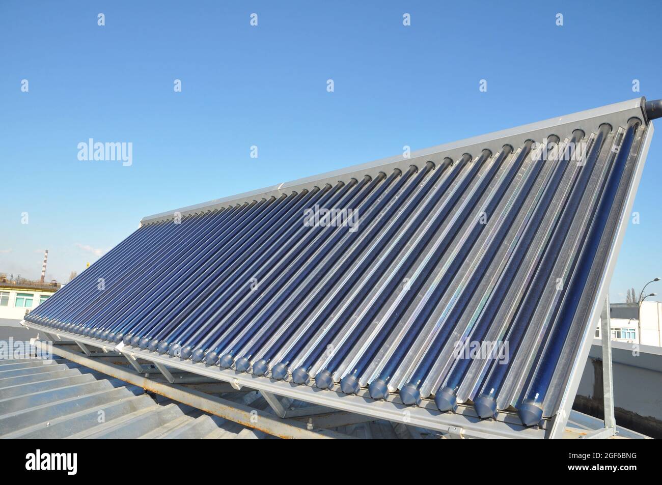 A close-up of an evacuated tube solar thermal hot water system, solar thermal panel collector installed on a metal roof against the blue sky. Stock Photo