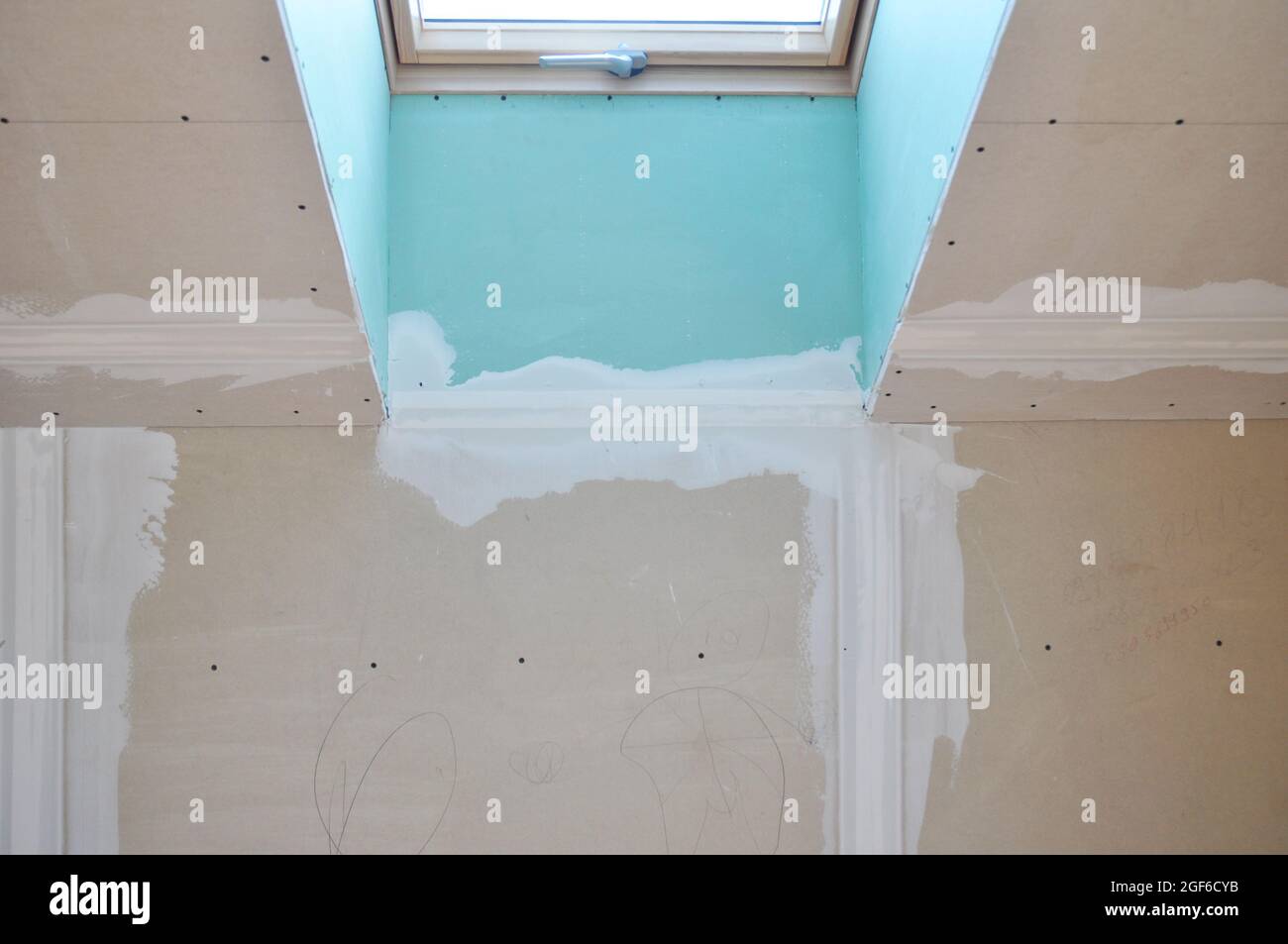 Installation of gypsum drywall boards around an attic skylight window applying a skim coat of compound to fill in the seams during the room renovation Stock Photo