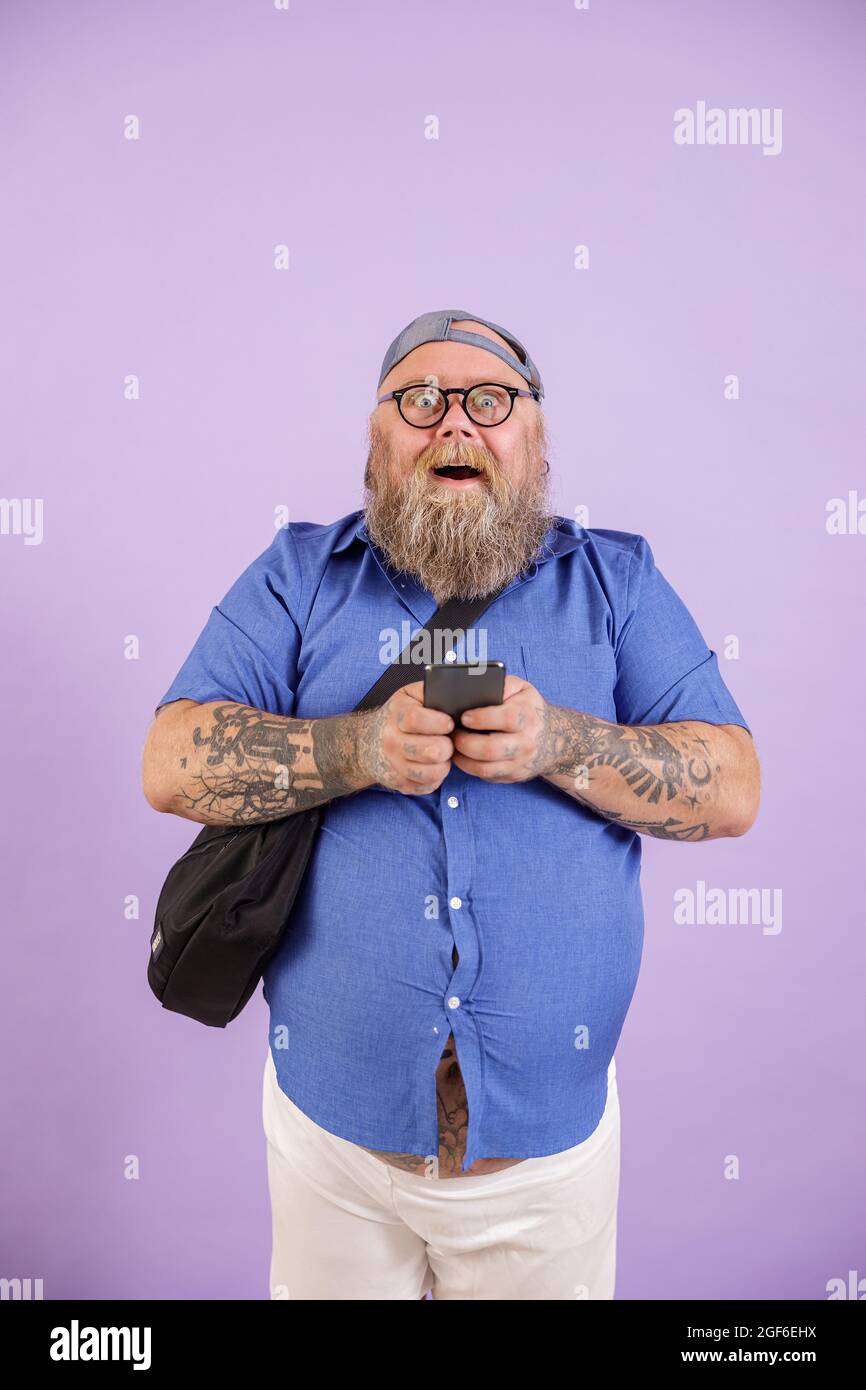 Funny plus size man with crossbody bag and glasses holds phone on