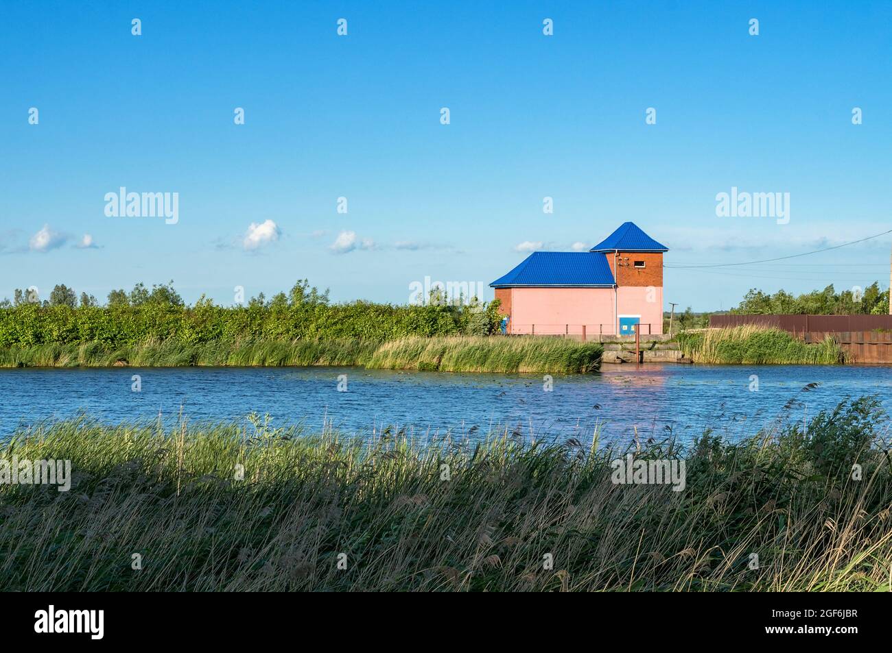 Little pink house on the river. The building is a pumping station. Technical building on the shore. Stock Photo