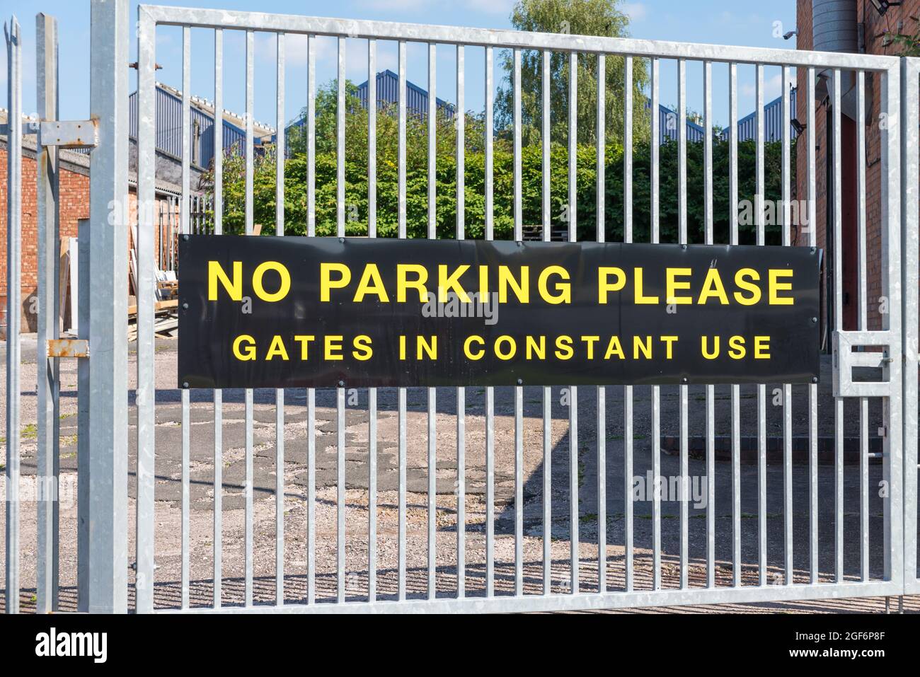 Large black and yellow sign on metal gate saying no parking please gate in constant use Stock Photo