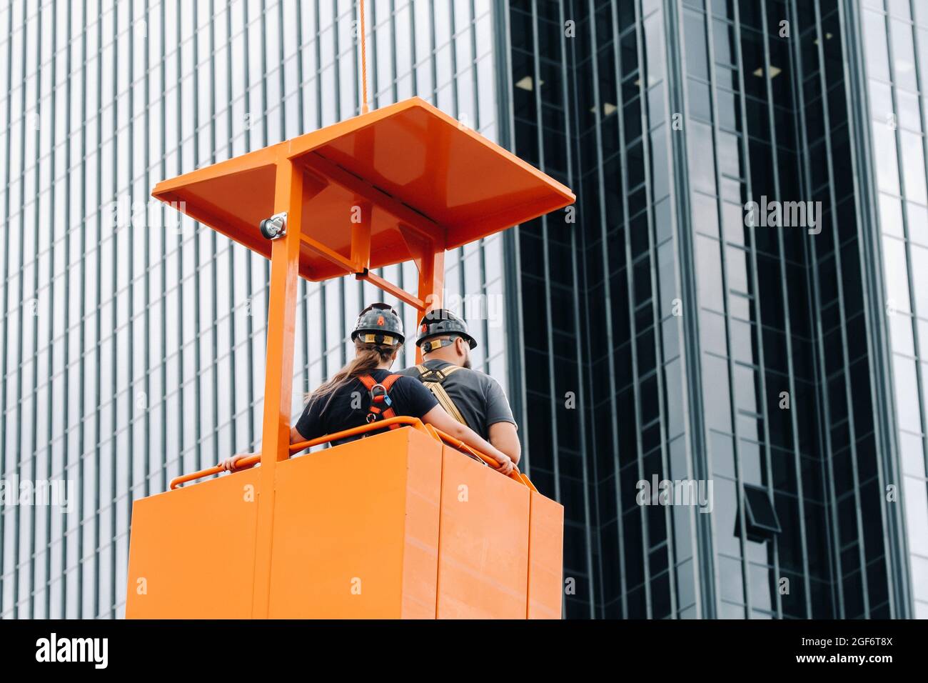 Workers in a construction cradle climb on a crane to a large glass
