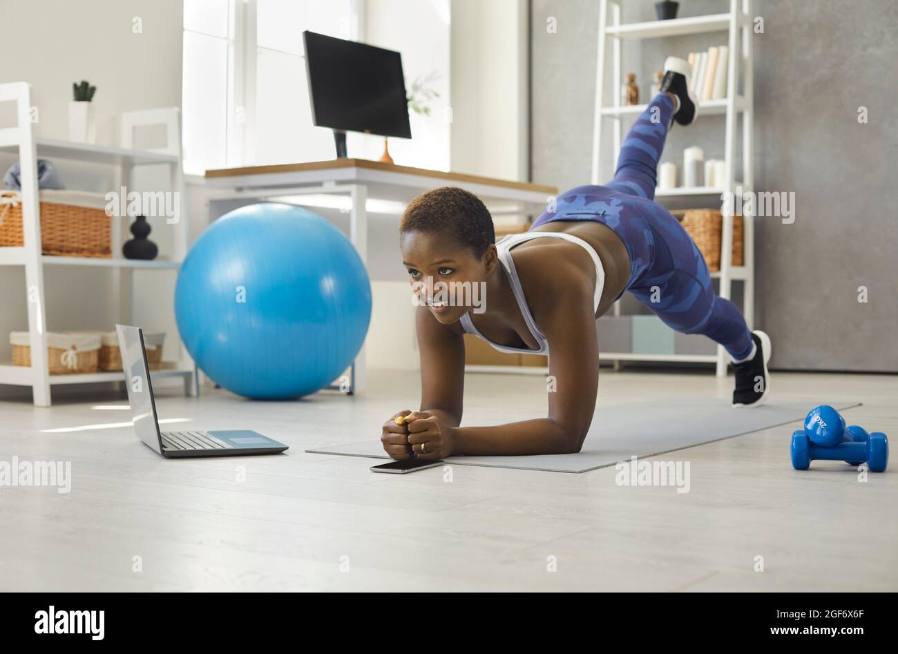 Woman doing sports exercises in front of laptop during online broadcast of fitness workout. Stock Photo