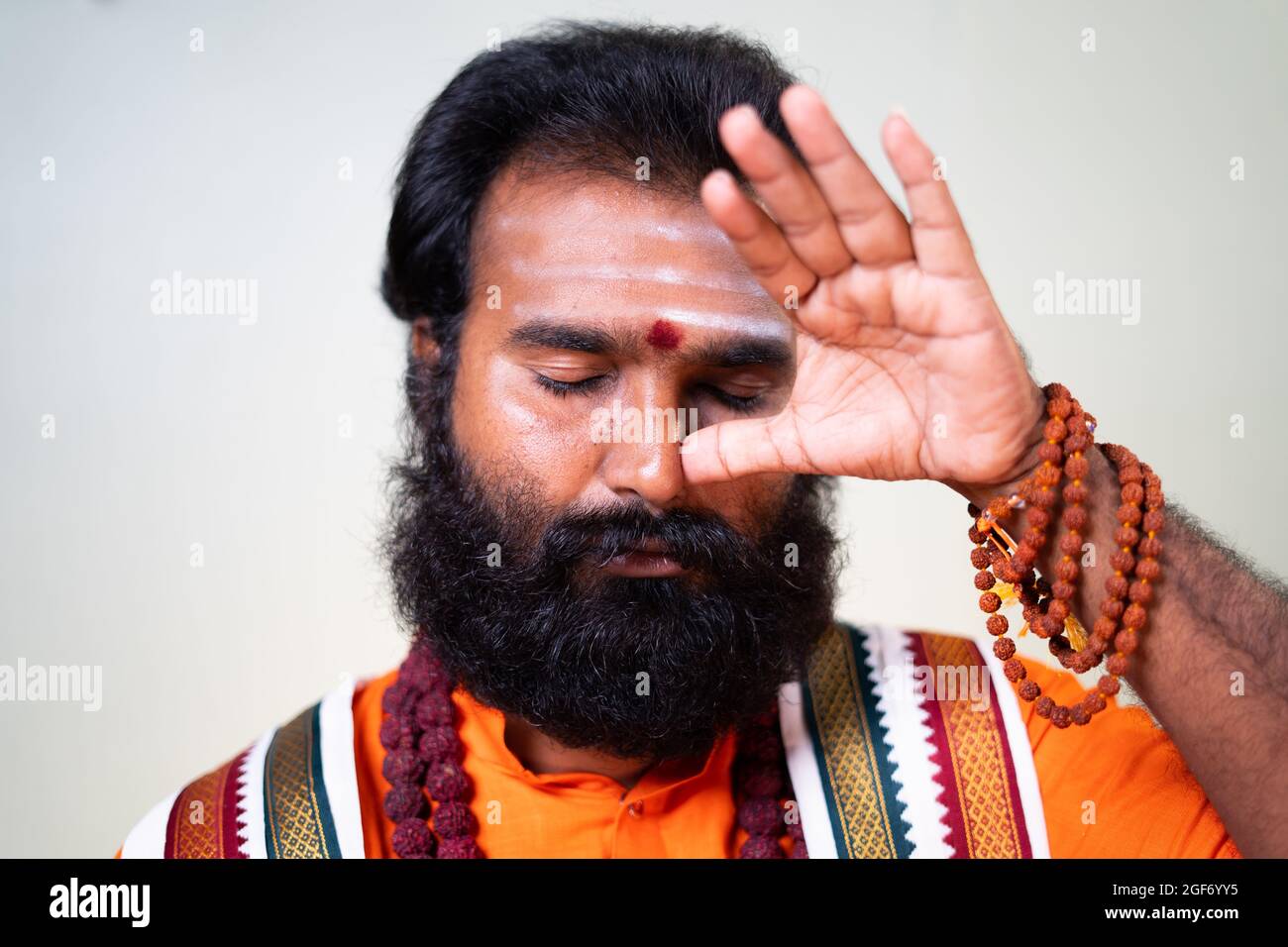 Close up head shot of Indian holy yoga guru or god man doing nostril breathing or nadi shodhana pranayama exercise or yoga. Stock Photo
