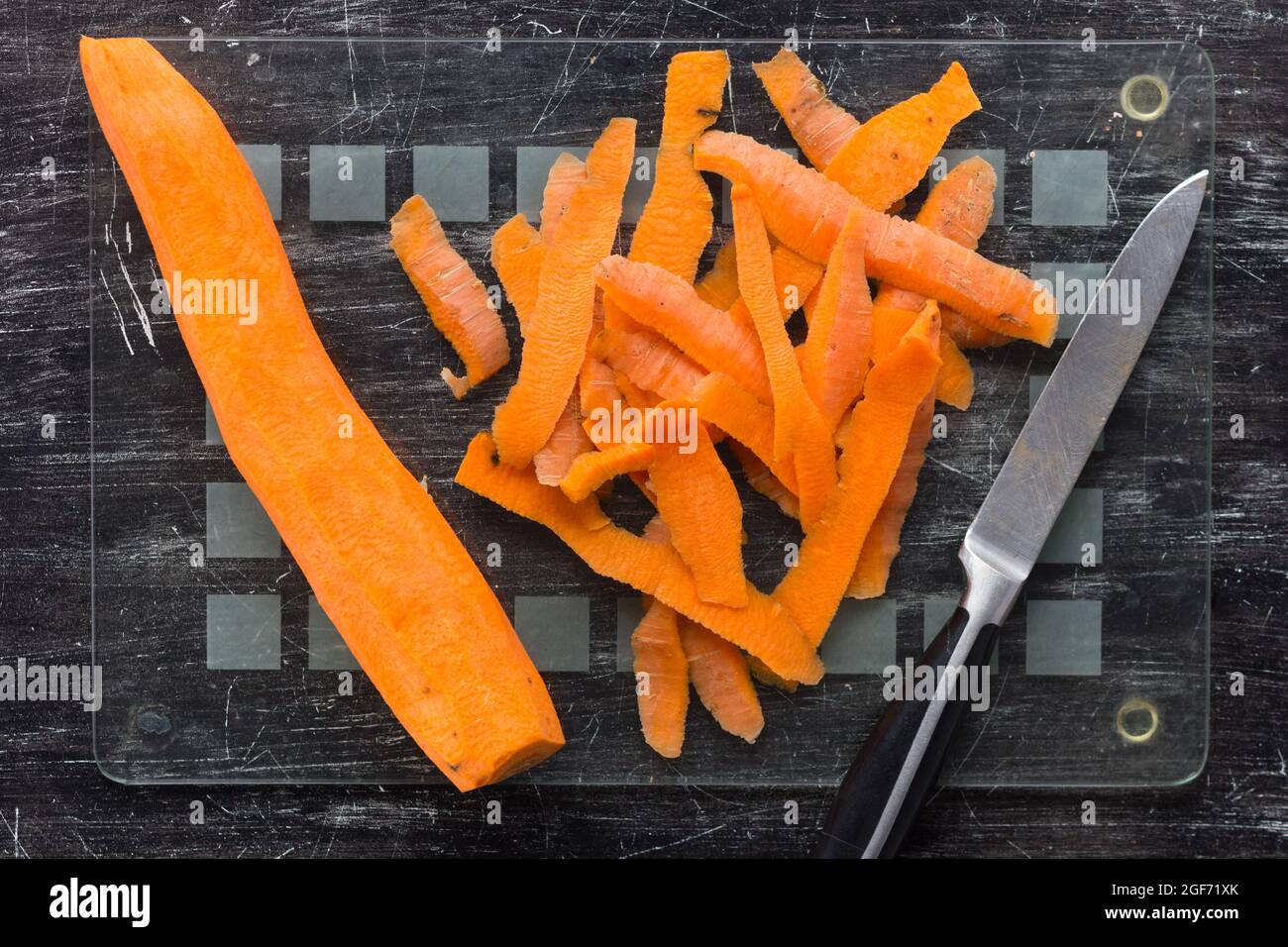 Top view of peeled carrot peeling, and knife on glass cutting board on