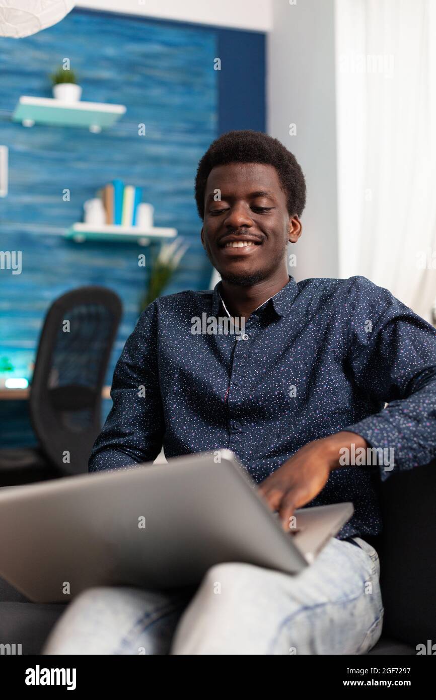 African american man typing on modern laptop computer relaxing on couch ...