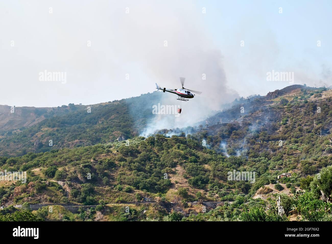 Fire helicopter dropping water from a bucket on a forest fire in the