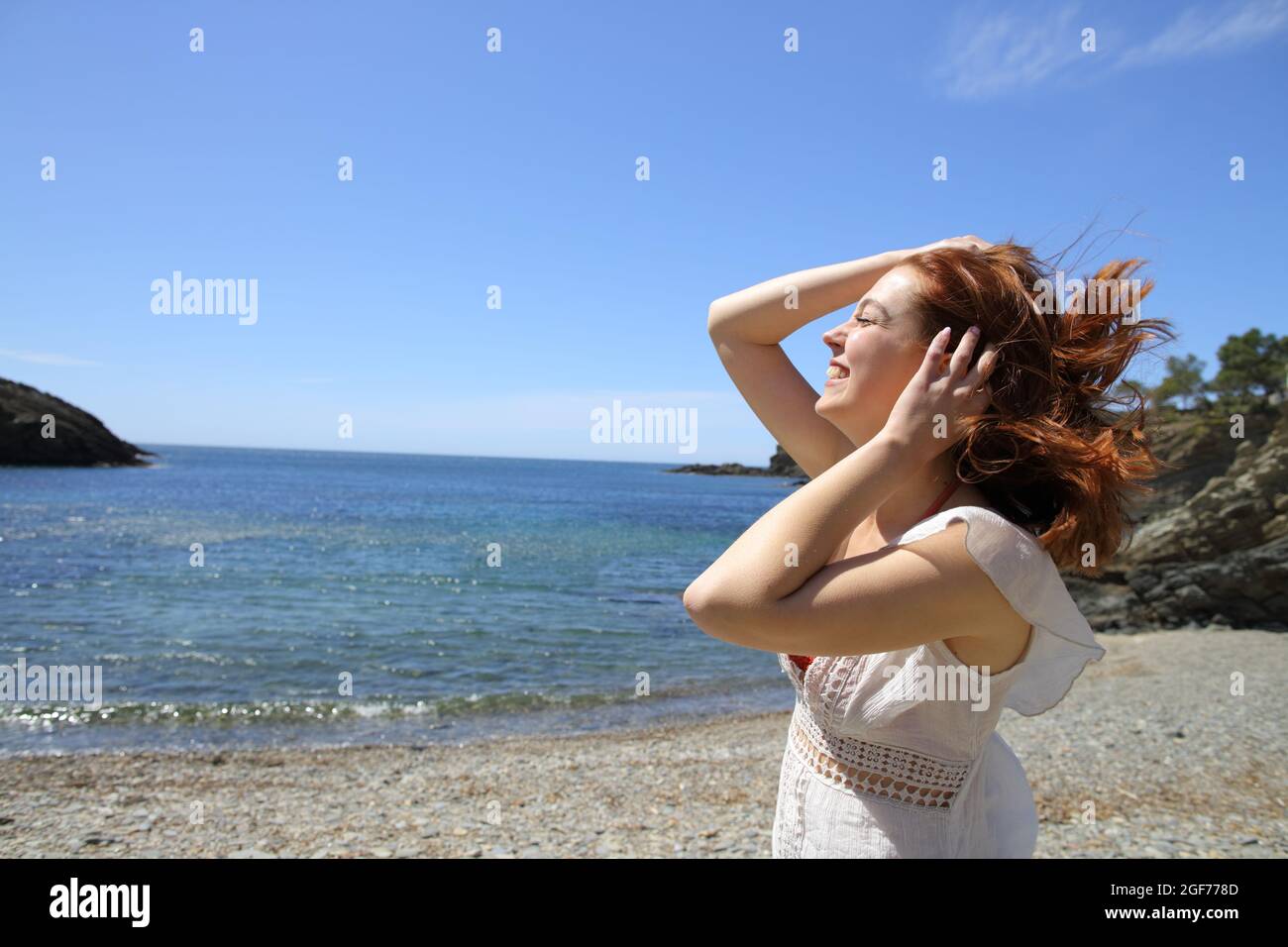 Happy woman touching tousled hair in a windy beach day on summer vacation Stock Photo